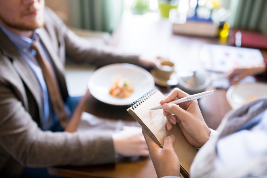 Close-up of waitress writing an order in her notepad with businessman sitting at the table in a cafe